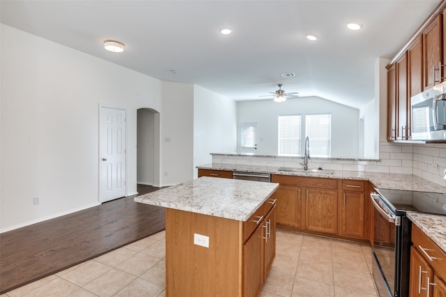 kitchen featuring a center island, lofted ceiling, ceiling fan, light wood-type flooring, and stainless steel appliances