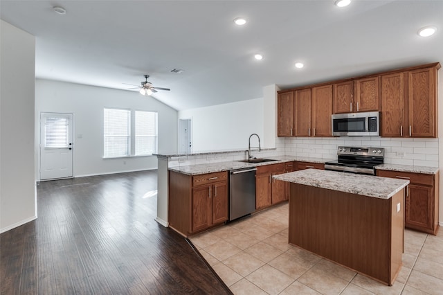 kitchen featuring sink, stainless steel appliances, light hardwood / wood-style flooring, kitchen peninsula, and vaulted ceiling