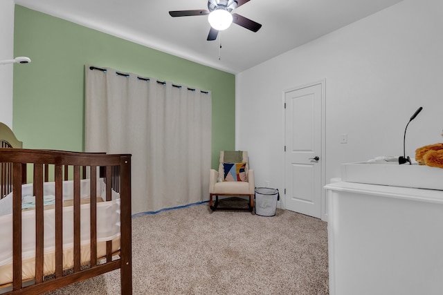 carpeted bedroom with ceiling fan and a crib