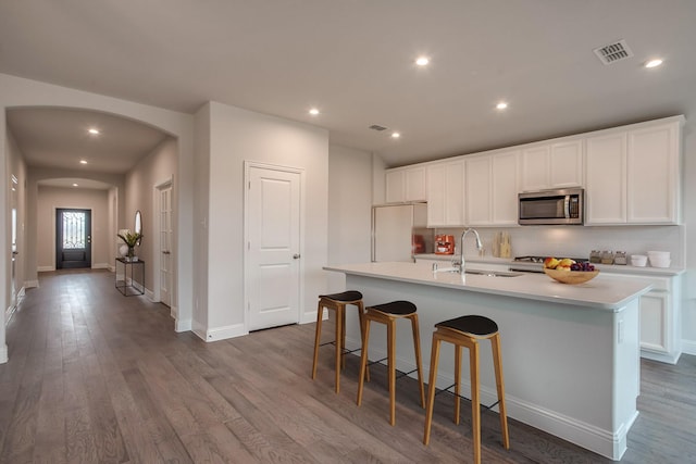 kitchen with white cabinets, wood-type flooring, an island with sink, sink, and fridge