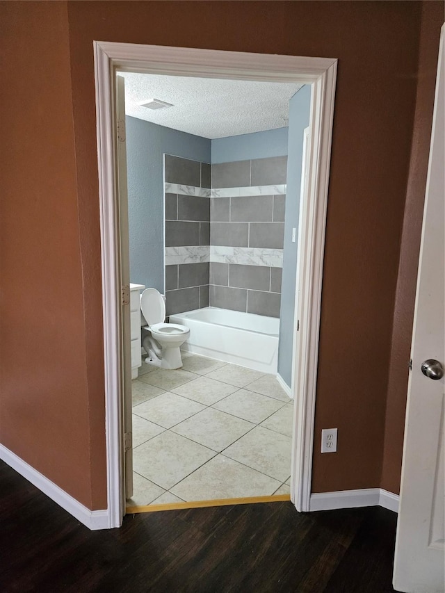 bathroom featuring a textured ceiling, toilet, and tiled shower / bath