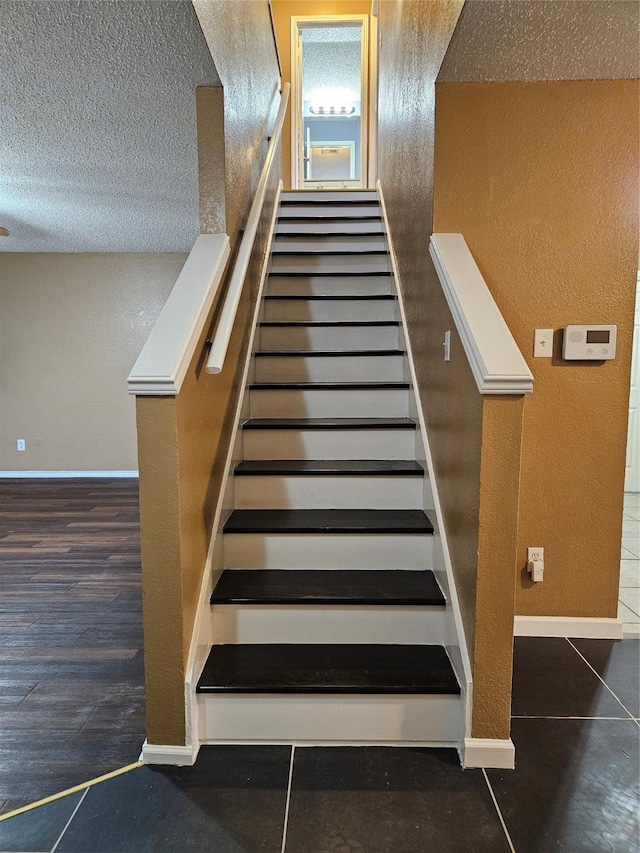 stairway with wood-type flooring and a textured ceiling