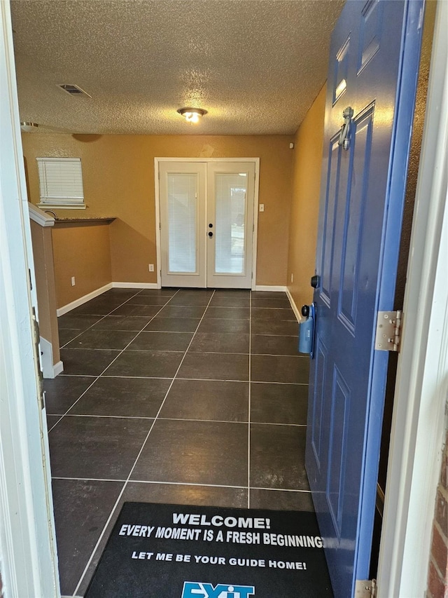 doorway with french doors, a textured ceiling, and dark tile patterned flooring