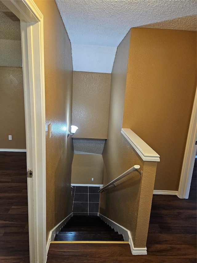 stairs with hardwood / wood-style floors, a textured ceiling, and vaulted ceiling