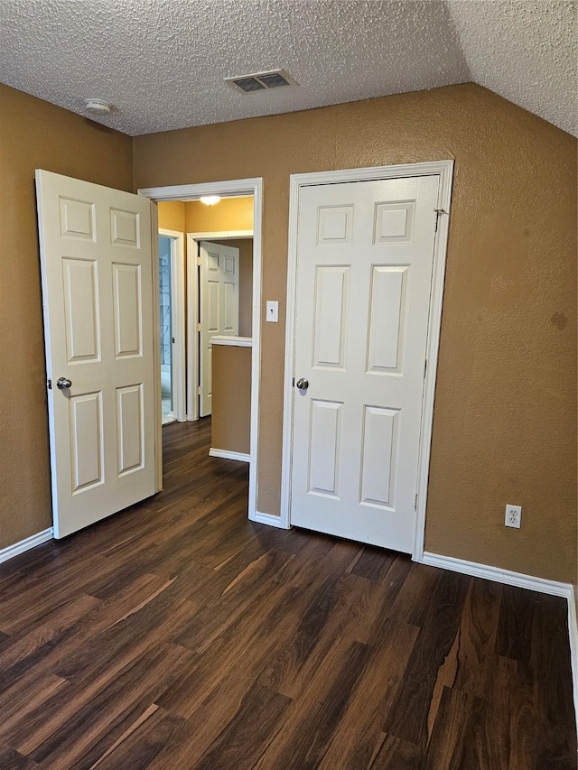 unfurnished bedroom featuring dark hardwood / wood-style flooring, a textured ceiling, and vaulted ceiling