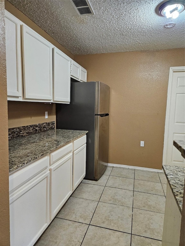 kitchen with stainless steel fridge, dark stone counters, a textured ceiling, light tile patterned floors, and white cabinetry