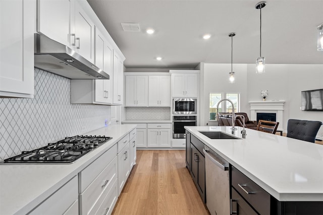 kitchen featuring a center island with sink, white cabinets, sink, light hardwood / wood-style flooring, and appliances with stainless steel finishes