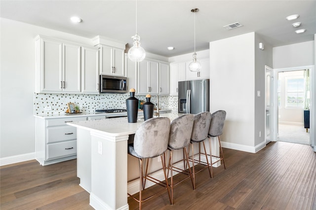 kitchen featuring decorative light fixtures, an island with sink, a breakfast bar area, white cabinets, and stainless steel appliances