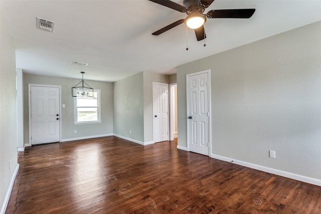 spare room with dark wood-type flooring and ceiling fan with notable chandelier