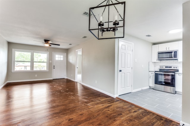 kitchen with decorative backsplash, appliances with stainless steel finishes, ceiling fan with notable chandelier, wood-type flooring, and white cabinets