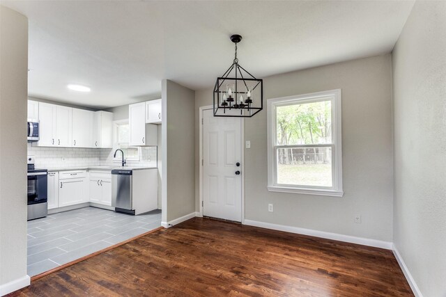 kitchen featuring white cabinetry, stainless steel appliances, pendant lighting, wood-type flooring, and decorative backsplash