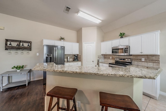 kitchen with a breakfast bar area, appliances with stainless steel finishes, light stone counters, white cabinets, and decorative backsplash