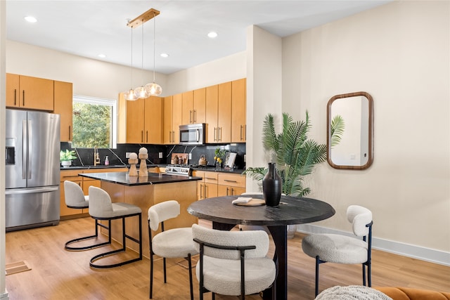 kitchen featuring a kitchen island, light brown cabinetry, sink, hanging light fixtures, and stainless steel appliances