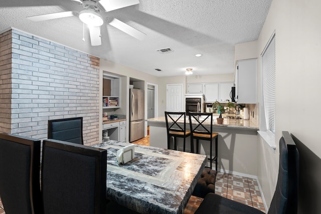 dining room featuring ceiling fan, a textured ceiling, and a brick fireplace