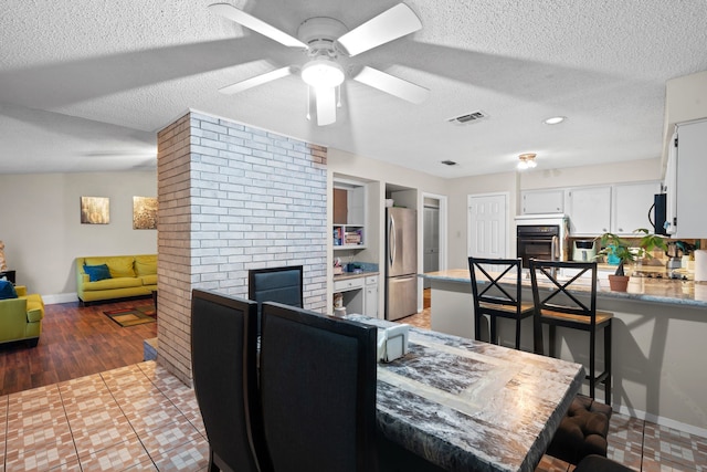 dining space featuring hardwood / wood-style floors, ceiling fan, a textured ceiling, and a brick fireplace