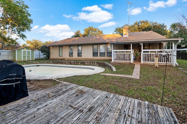 back of house featuring a lawn, a pool side deck, and a storage shed