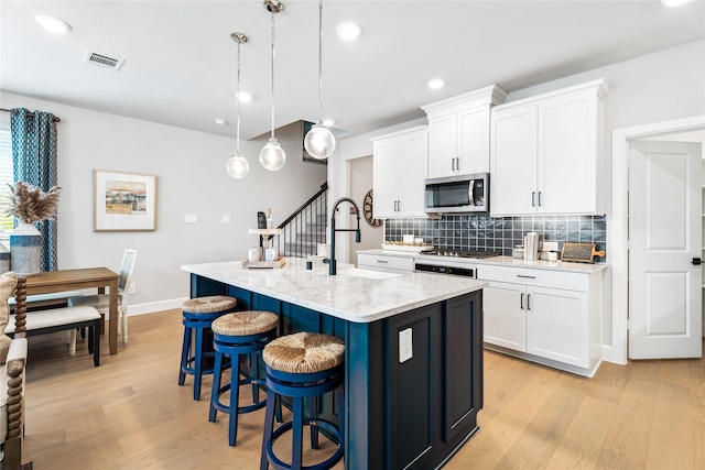 kitchen featuring hanging light fixtures, an island with sink, appliances with stainless steel finishes, and white cabinetry