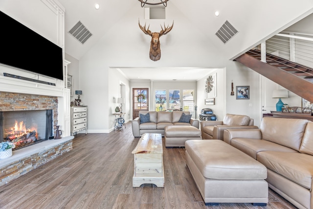 living area featuring visible vents, a stone fireplace, wood finished floors, high vaulted ceiling, and baseboards