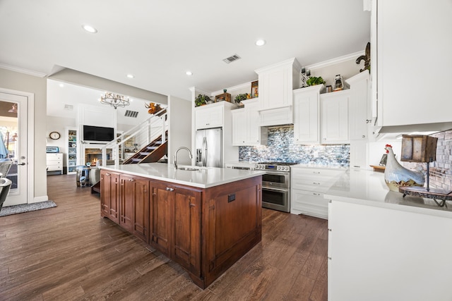 kitchen with stainless steel appliances, visible vents, light countertops, an island with sink, and crown molding