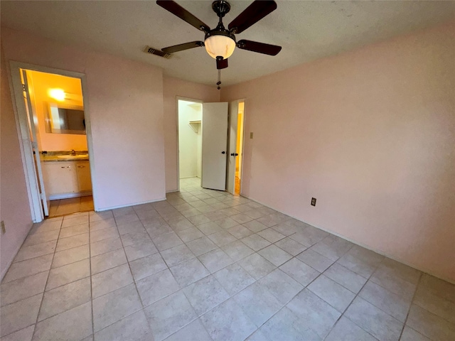 unfurnished bedroom with light tile patterned floors, ensuite bathroom, and ceiling fan