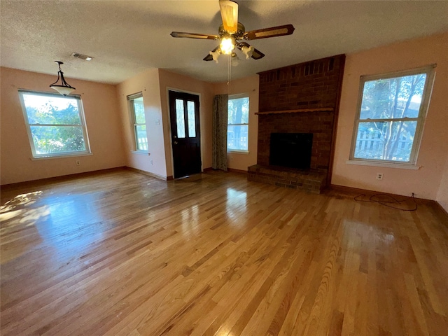 unfurnished living room featuring a fireplace, a textured ceiling, light hardwood / wood-style floors, and ceiling fan