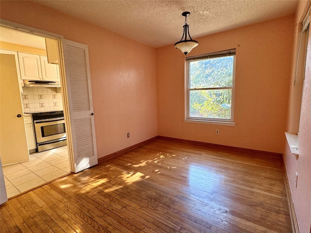 unfurnished dining area with a textured ceiling and light wood-type flooring