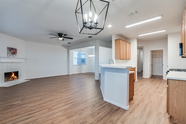 kitchen with a tile fireplace, ceiling fan with notable chandelier, light brown cabinetry, light hardwood / wood-style floors, and kitchen peninsula