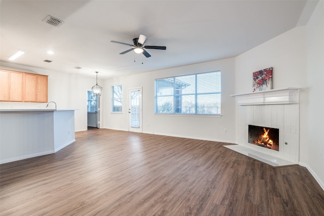 unfurnished living room featuring ceiling fan with notable chandelier, dark wood-type flooring, and a tiled fireplace