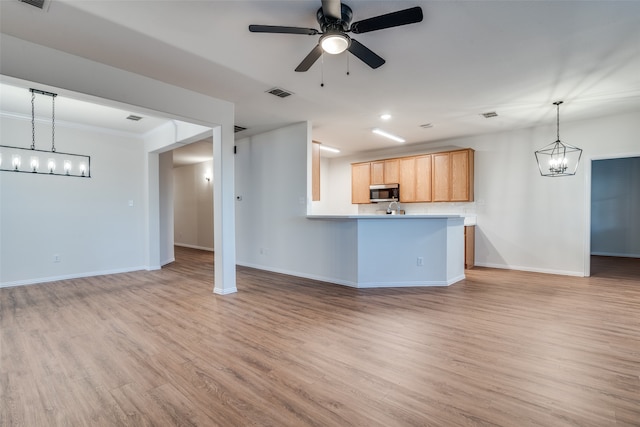 unfurnished living room featuring ceiling fan with notable chandelier and light hardwood / wood-style flooring