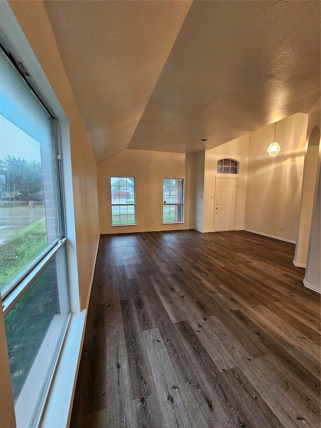 unfurnished living room with a textured ceiling, vaulted ceiling, and dark wood-type flooring