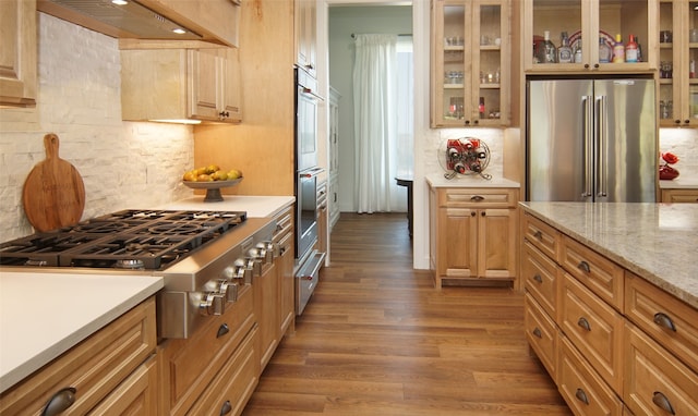 kitchen featuring premium range hood, appliances with stainless steel finishes, tasteful backsplash, dark hardwood / wood-style flooring, and light stone counters