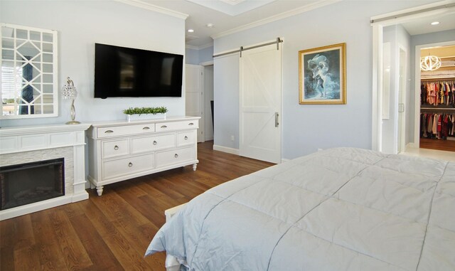 bedroom featuring dark wood-type flooring, a stone fireplace, a barn door, ornamental molding, and a closet