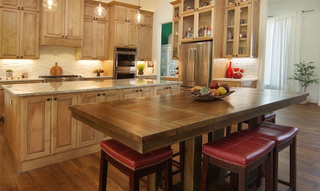 kitchen with light stone countertops, hanging light fixtures, dark hardwood / wood-style floors, and appliances with stainless steel finishes