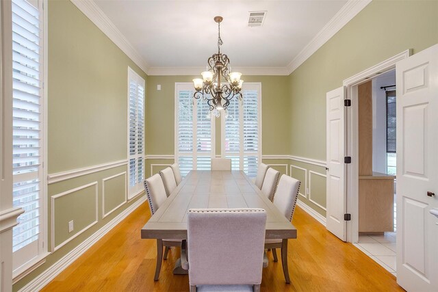 dining space with crown molding, light hardwood / wood-style floors, and an inviting chandelier