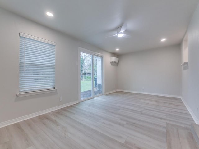 empty room featuring light wood finished floors, ceiling fan, baseboards, and a wall unit AC