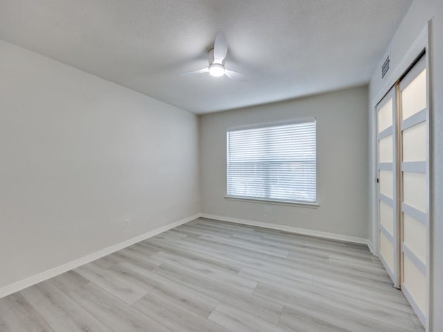 empty room with baseboards, light wood-style floors, a ceiling fan, and a textured ceiling