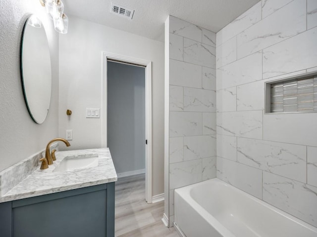 bathroom with hardwood / wood-style floors, vanity, tiled shower / bath combo, and a textured ceiling