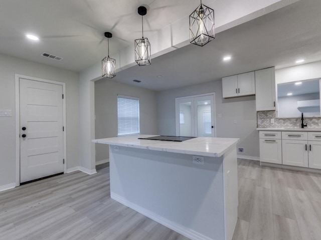 kitchen with decorative backsplash, light wood finished floors, hanging light fixtures, and white cabinetry