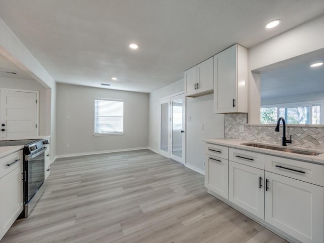 kitchen with a sink, backsplash, white cabinetry, stainless steel range with electric cooktop, and light wood finished floors