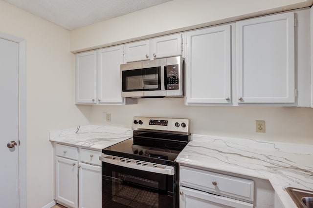 kitchen featuring light stone counters, stainless steel appliances, a textured ceiling, and white cabinets