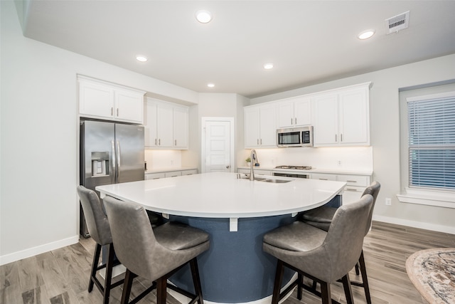 kitchen with white cabinets, appliances with stainless steel finishes, light wood-type flooring, and an island with sink