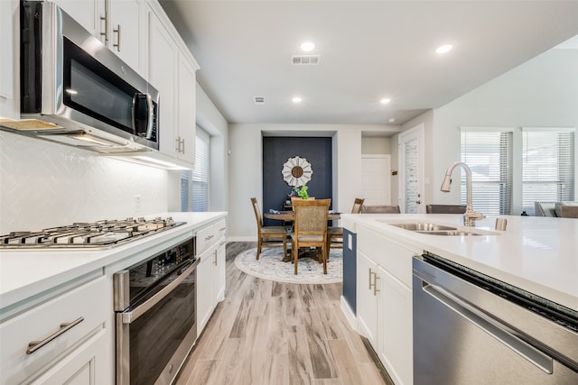 kitchen with white cabinets, sink, appliances with stainless steel finishes, and light hardwood / wood-style flooring