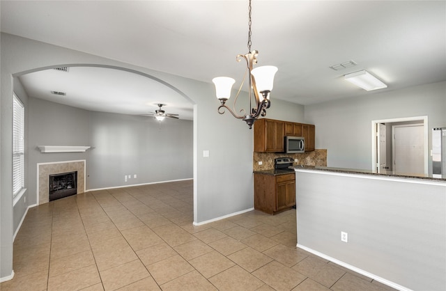 kitchen featuring hanging light fixtures, appliances with stainless steel finishes, a tile fireplace, ceiling fan with notable chandelier, and decorative backsplash