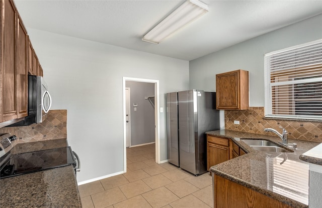 kitchen featuring appliances with stainless steel finishes, tasteful backsplash, sink, dark stone counters, and light tile patterned floors