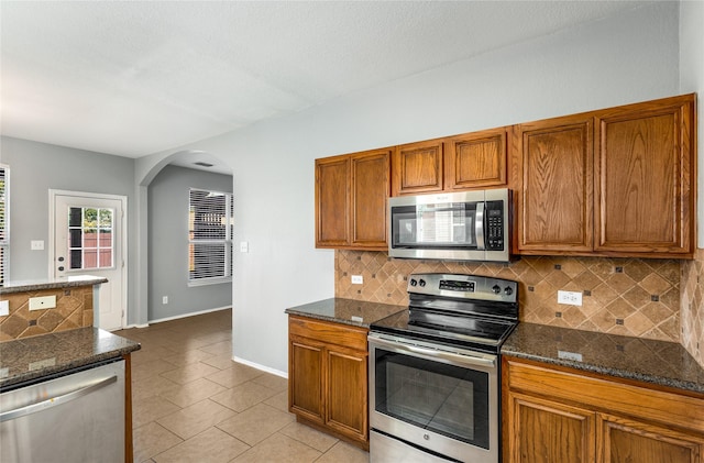 kitchen featuring dark stone countertops, light tile patterned floors, decorative backsplash, and stainless steel appliances