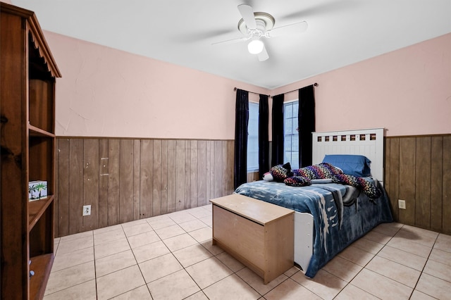 bedroom featuring ceiling fan, light tile patterned floors, and wooden walls