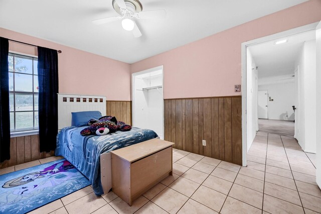 bedroom featuring wooden walls, ceiling fan, a spacious closet, light tile patterned floors, and a closet