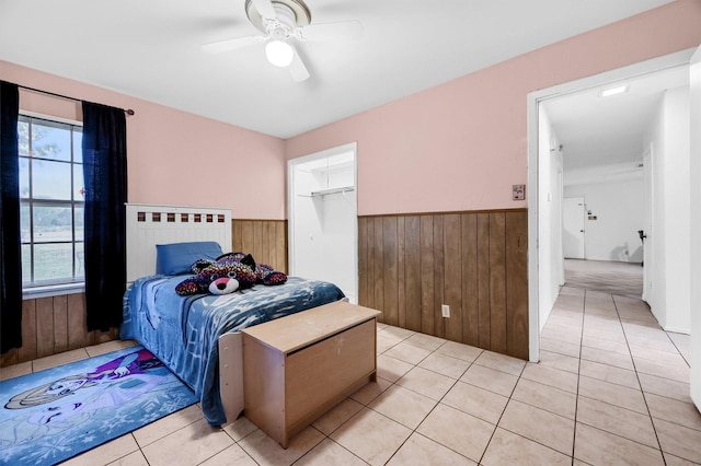 tiled bedroom with wooden walls, a closet, and ceiling fan