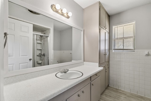 bathroom with hardwood / wood-style floors, toilet, vanity, a shower with shower door, and tile walls