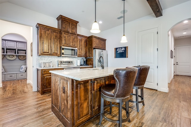 kitchen featuring a kitchen island with sink, hanging light fixtures, sink, appliances with stainless steel finishes, and light hardwood / wood-style floors